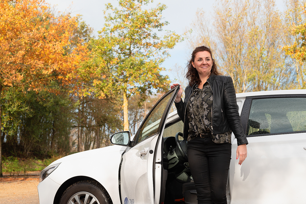 Vrouw stapt uit witte auto in herfstomgeving